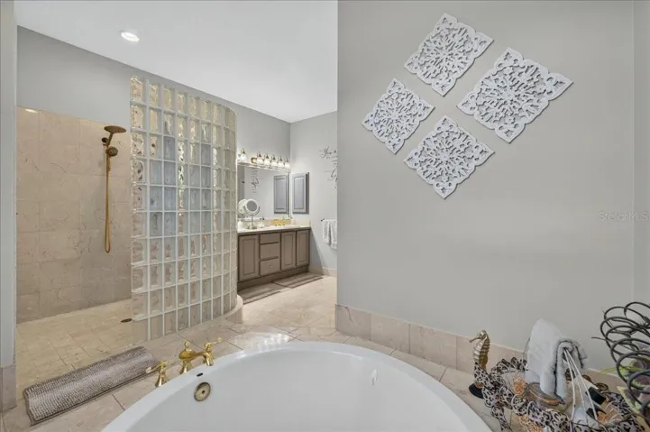 The ensuite bath offers extensive marble finishes, soaking tub, an oversized shower with a curved glass-block wall, double-sink vanity, and a separate water closet with bidet.