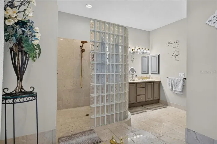 The ensuite bath offers extensive marble finishes, soaking tub, an oversized shower with a curved glass-block wall, double-sink vanity, and a separate water closet with bidet.