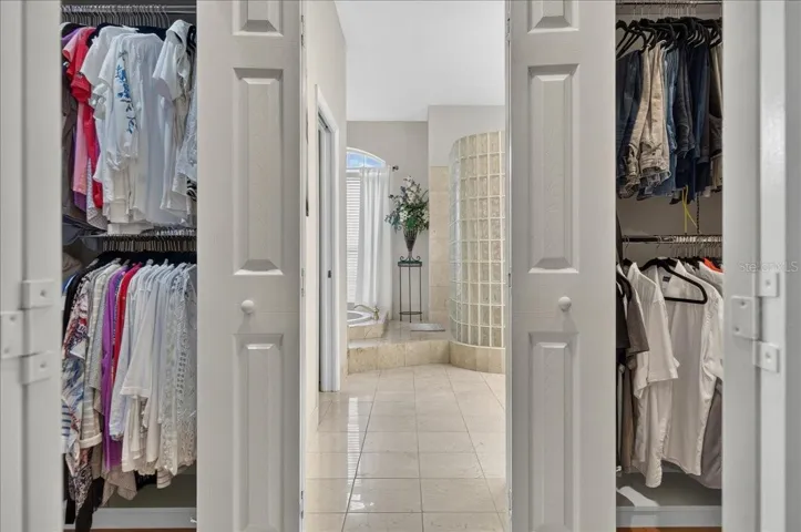 The primary bedroom retreat is set apart within the split-bedroom plan and features a transom window and French doors to the lanai and views beyond. Two walk-in closets with built-in organizers provide generous storage