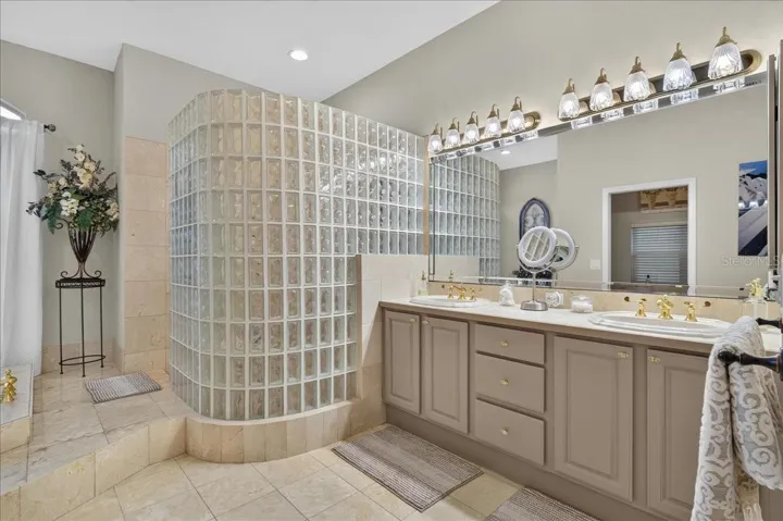 The ensuite bath offers extensive marble finishes, soaking tub, an oversized shower with a curved glass-block wall, double-sink vanity, and a separate water closet with bidet.