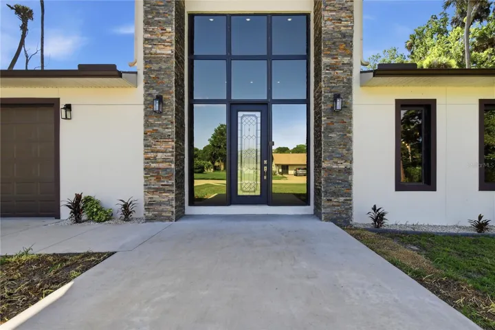 A soaring front entry with expansive floor-to-ceiling glass welcomes abundant natural light into the home, highlighting the modern architecture while creating an elegant and airy ambiance throughout the main living space.