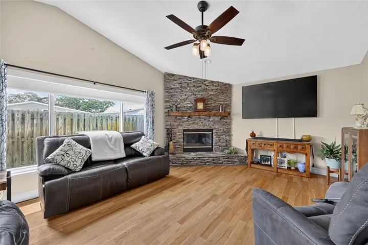 THe family room has a wood burning fireplace, ceiling fan and large picture window