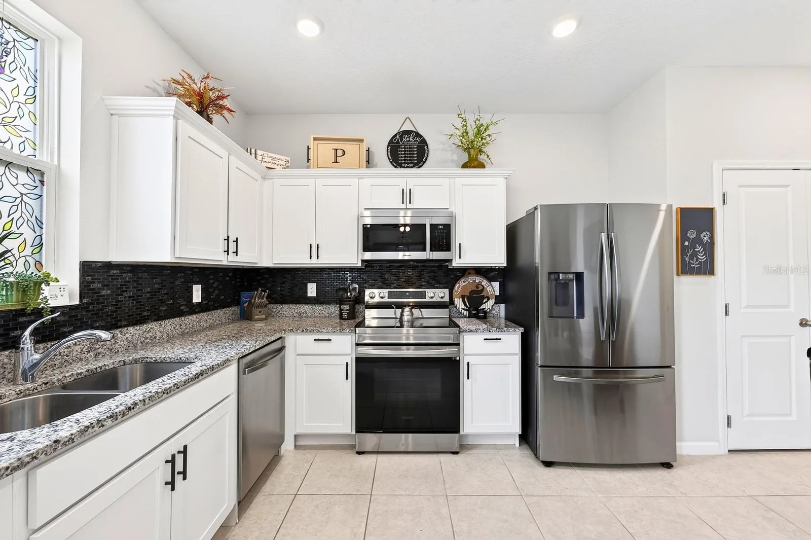 The bright, modern Kitchen is the heart of the home, featuring crisp white cabinetry, GRANITE COUNTERTOPS, stainless steel appliances, a stylish tile backsplash, recessed lighting, and a convenient closet pantry.