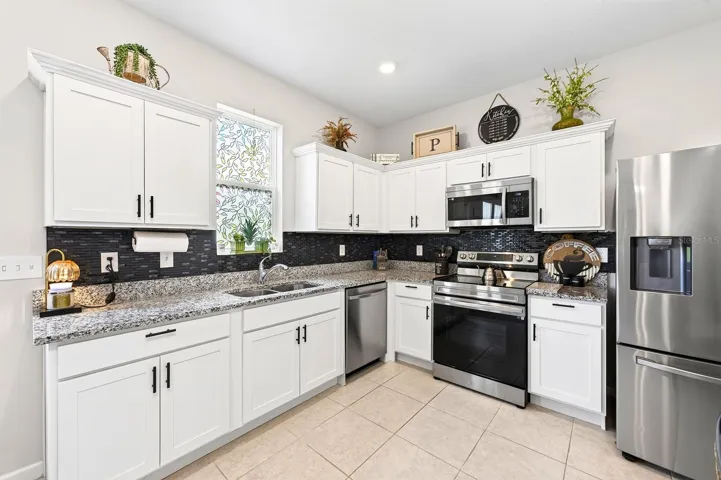 The bright, modern Kitchen is the heart of the home, featuring crisp white cabinetry, GRANITE COUNTERTOPS, stainless steel appliances, a stylish tile backsplash, recessed lighting, and a convenient closet pantry.
