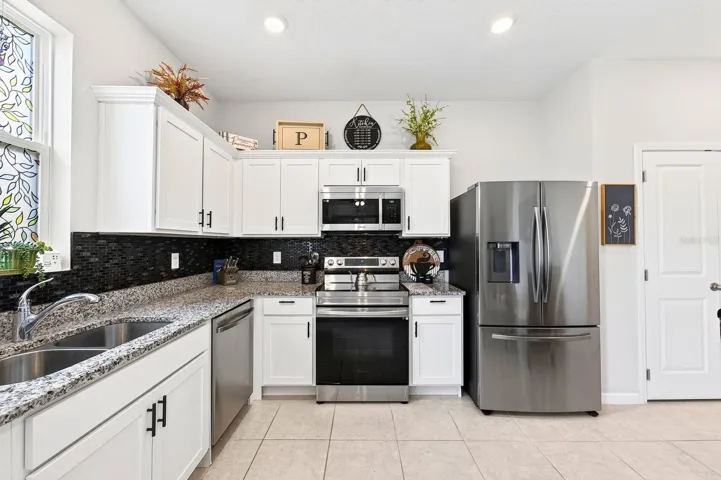 The bright, modern Kitchen is the heart of the home, featuring crisp white cabinetry, GRANITE COUNTERTOPS, stainless steel appliances, a stylish tile backsplash, recessed lighting, and a convenient closet pantry.
