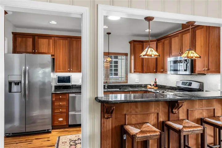 Kitchen with bar seating, stainless steel appliances, wood cabinetry and pendant lighting