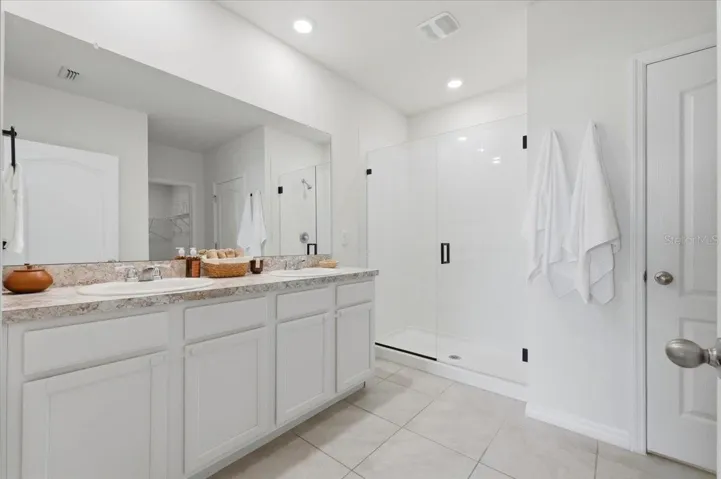 Ensuite bathroom connected to the primary bedroom, featuring a dual-sink vanity and a walk-in standing shower with sleek glass doors.