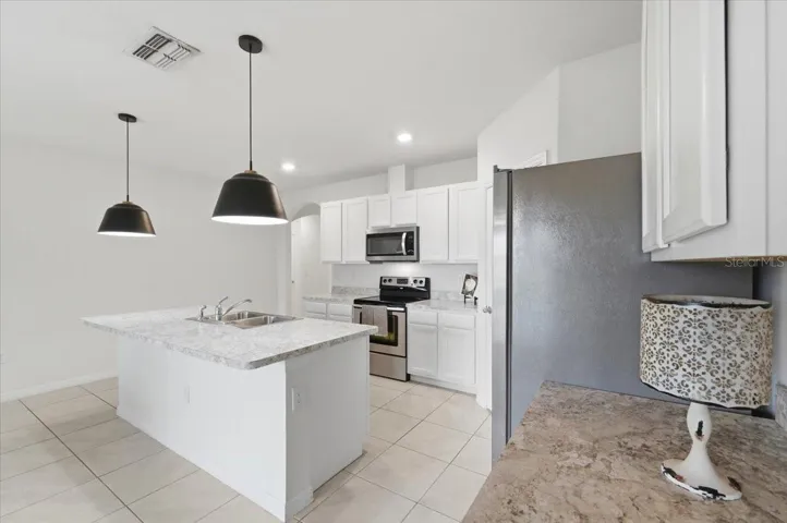 This kitchen features sleek stainless steel appliances, an oversized central island topped with elegant granite, and an open-concept layout that seamlessly overlooks the dining and living areas, perfect for entertaining.