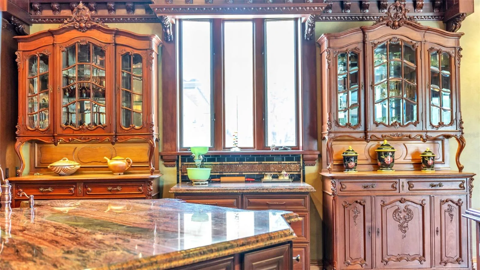 Anchored by Twin Antique Hutches, the kitchen features stately Symmetrical millwork, Exotic Solarious Natural Stone Island. Every slab features dramatic swirling veins, creating a living piece of art across the counters.