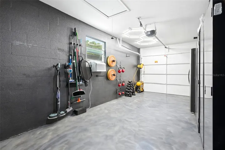 Immaculate garage with a finished epoxy floor, A/C unit, double utility sink, and pull down attic stairs