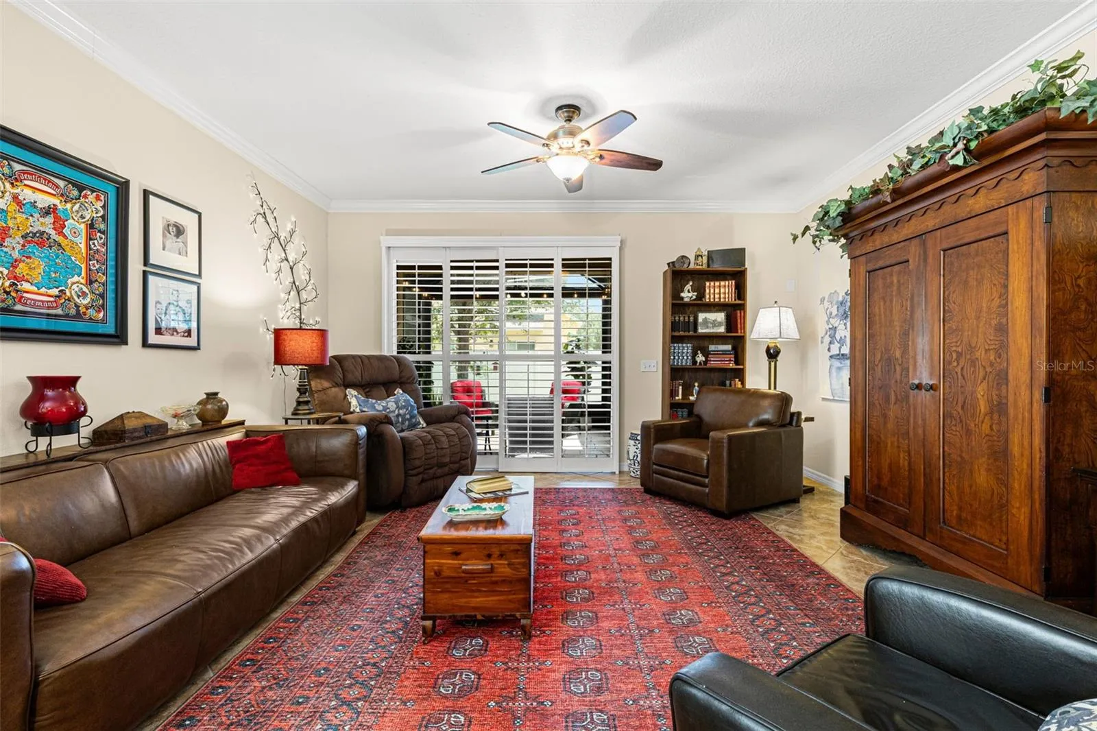 The living room has room for full-size furnishings, with crown molding, a ceiling fan and plantation shutters across the doors to the screened lanai.
