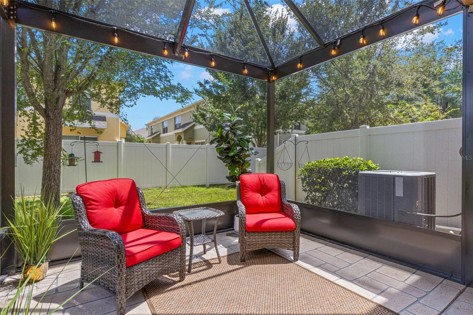 The screened lanai overlooks a small grassy area framed by a vinyl privacy fence and mature trees, adding a welcome sense of separation from neighboring homes.