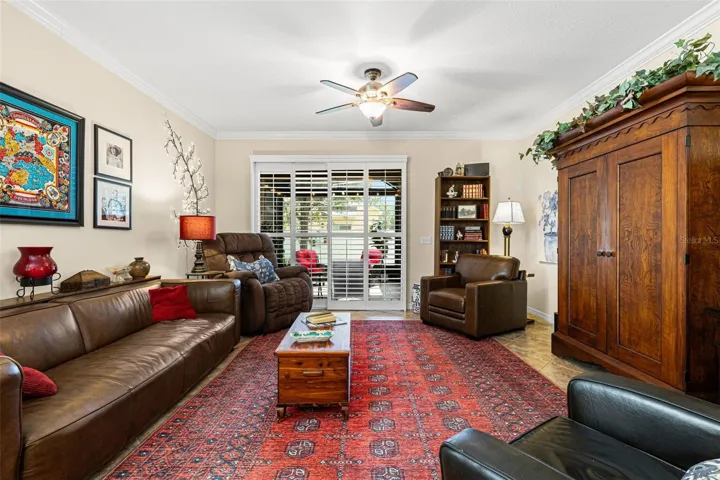 The living room has room for full-size furnishings, with crown molding, a ceiling fan and plantation shutters across the doors to the screened lanai.