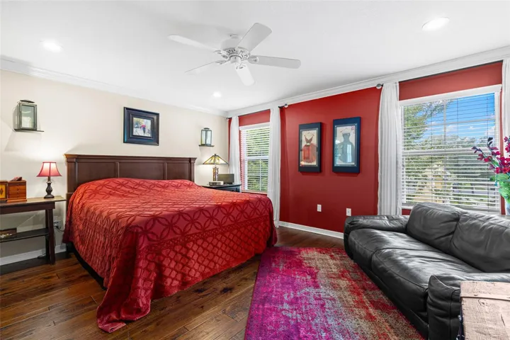 The spacious primary bedroom offers hardwood flooring, a ceiling fan and room for a sitting area, with three windows bringing in plenty of natural light.