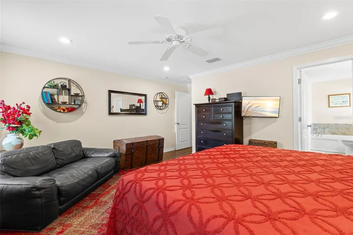 Another view of the primary suite highlights its generous proportions, hardwood flooring, crown molding and direct access to the en suite bath.