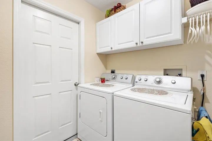 Inside laundry room with overhead cabinets, two car garage through the door to left of dryer.