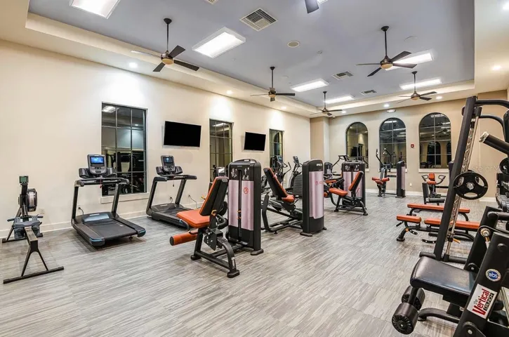Floor-to-ceiling windows and multiple ceiling fans keep the community fitness center bright and airy, outfitted with a full lineup of treadmills, ellipticals, strength machines, and free weights. Mirrored walls and wood-look flooring round out a space built for a complete workout without leaving the neighborhood.