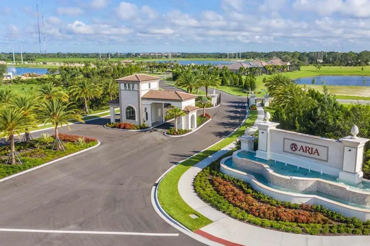 An aerial perspective takes in Aria's full entry sequence, from the fountain-flanked monument sign to a covered gatehouse-style structure and winding entry drive, framed by lakes and lush landscaping. The layout offers a clear sense of the community's scale and setting.