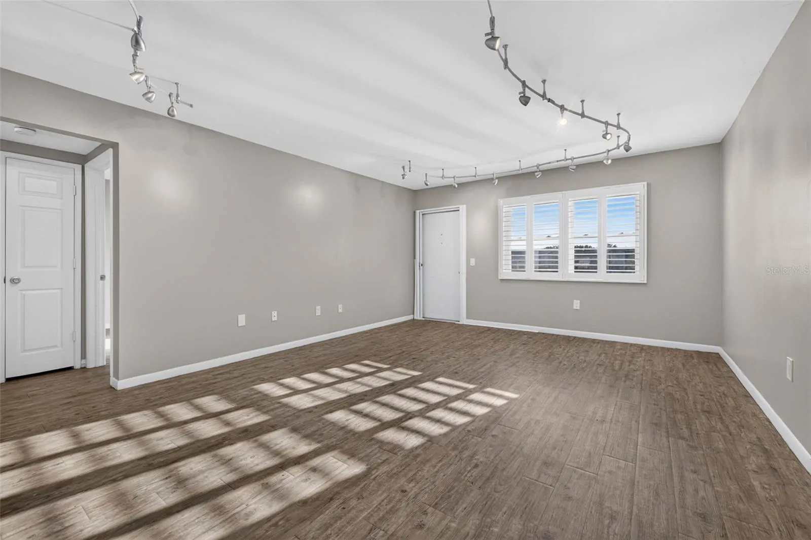 Bright, spacious living room featuring luxury vinyl flooring, plantation shutters, modern track lighting, and an open layout perfect for everyday living and entertaining.