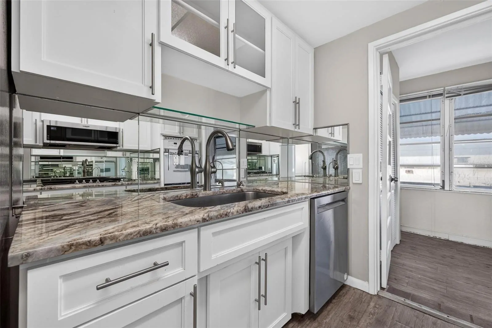 Kitchen with white shaker cabinets, mirrored backsplash, stainless steel appliances, abundant counter space, and modern finishes.