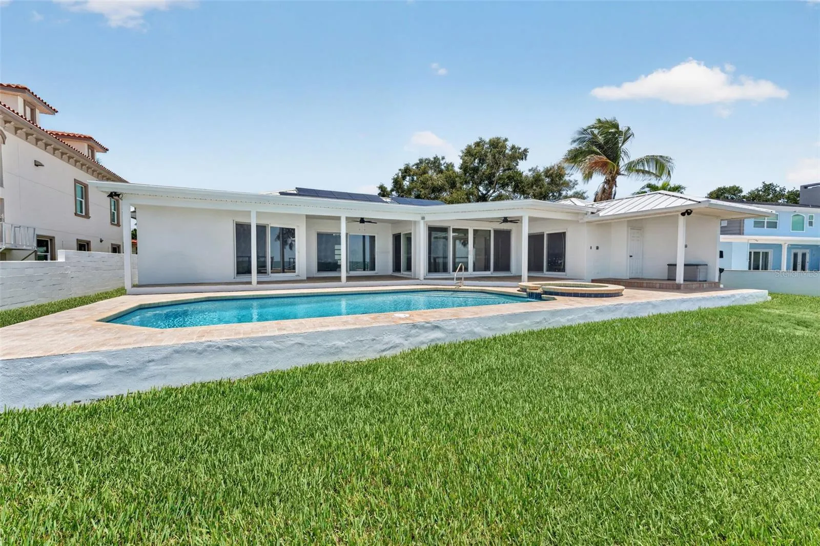 Beautiful outdoor space viewed from the seawall, showcasing the pool, patio, and backyard leading up to the home.