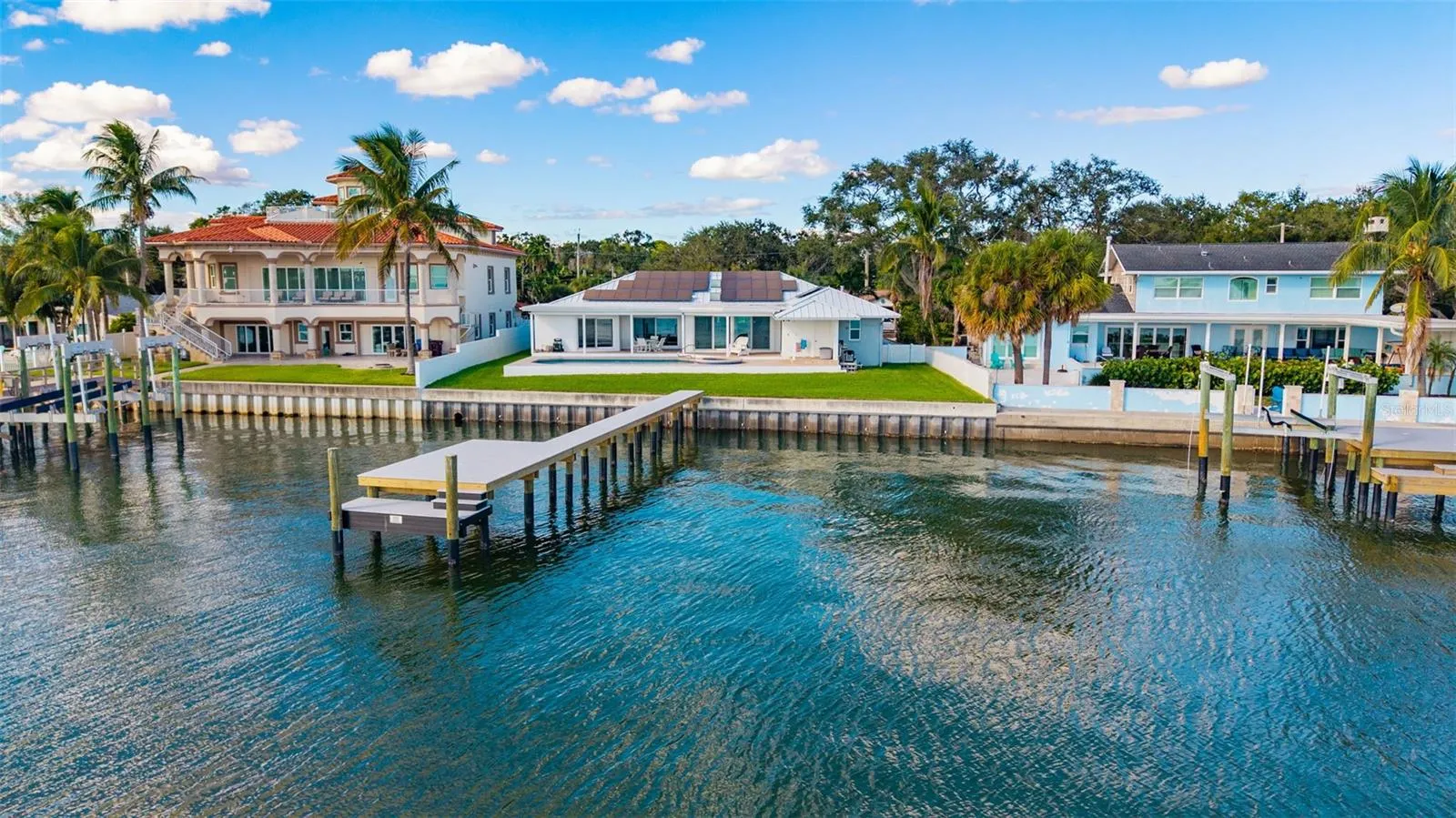 Drone view from the water highlighting the backyard, pool, home, and newly installed dock, all set against stunning waterfront scenery.