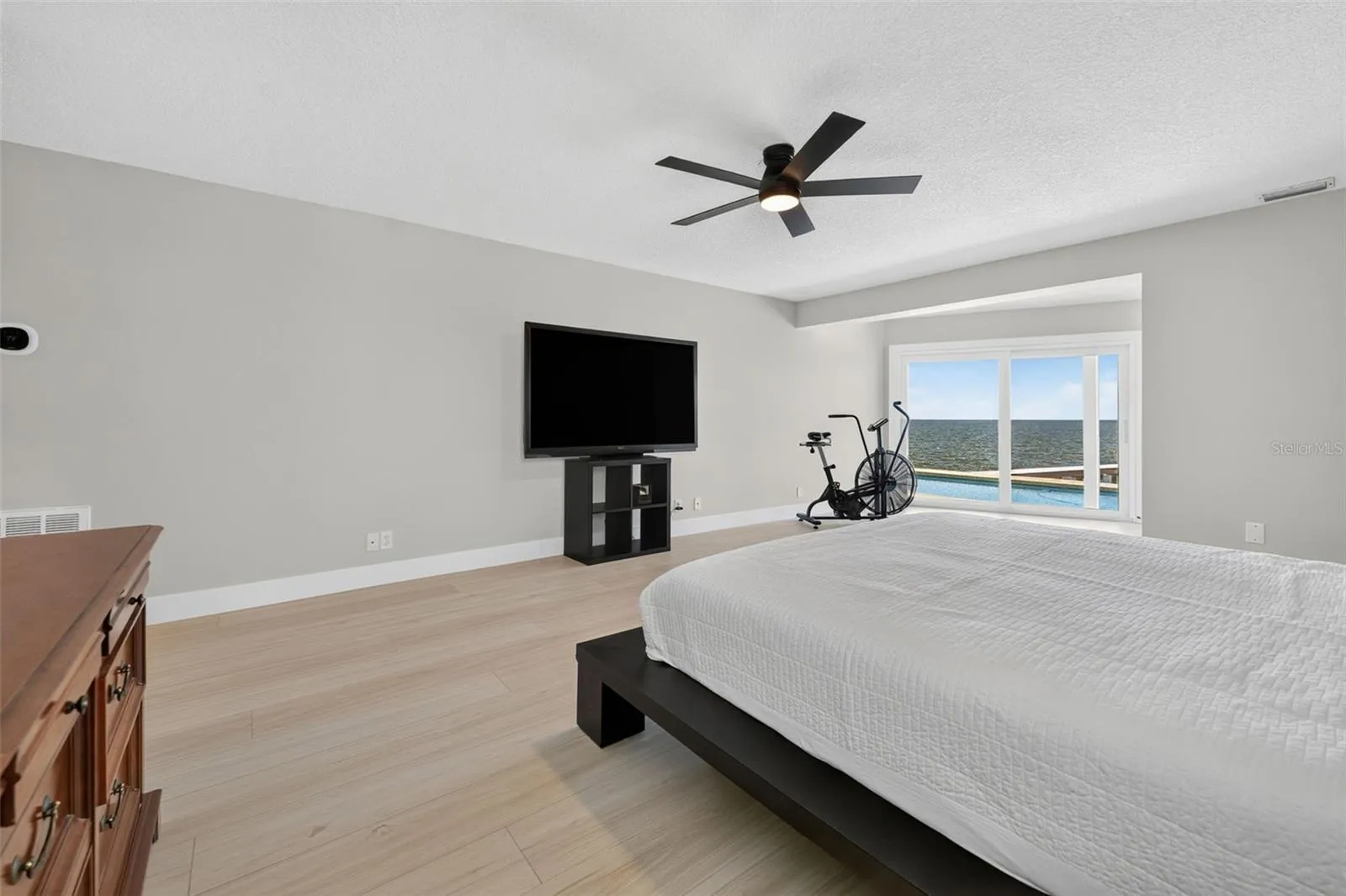 Expansive primary bedroom with sliding glass doors that open to the pool deck and showcase stunning waterfront views.