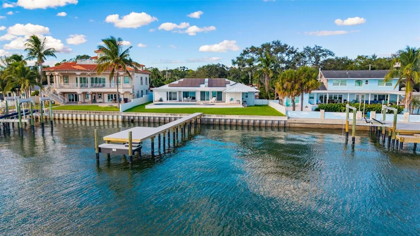 Drone view from the water highlighting the backyard, pool, home, and newly installed dock, all set against stunning waterfront scenery.