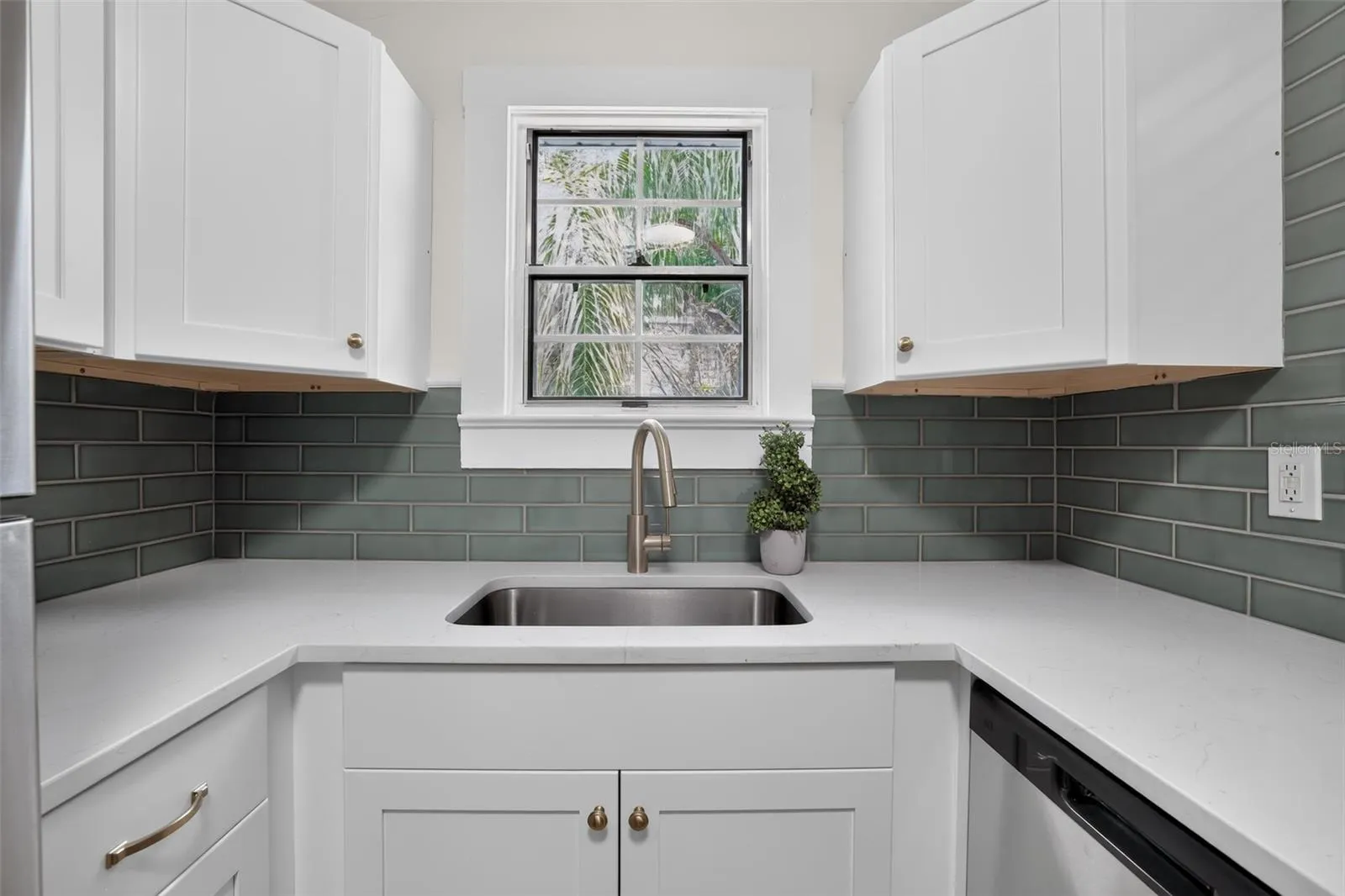 Bright kitchen sink area with quartz counters and soft green tile in this 1922 bungalow