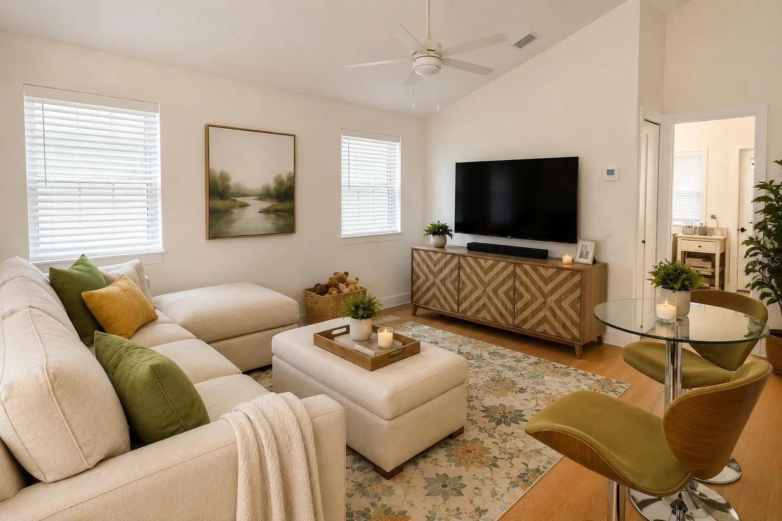 Inviting living room with vaulted ceilings, rich real wood floors, crisp white walls, a ceiling fan, and abundant windows that fill the space with natural light.