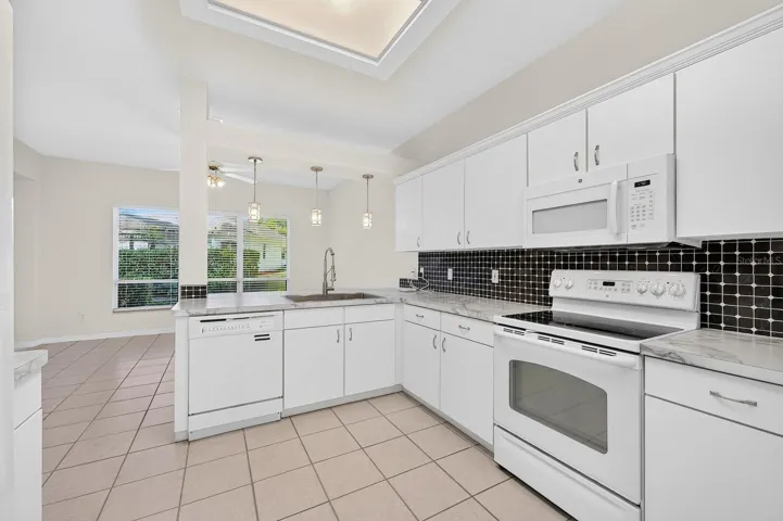The spacious Kitchen, REFRESHED IN 2024, offers plenty to appreciate, including newer countertops, updated cabinet hardware and crown molding, a newer large sink and a tile backsplash.