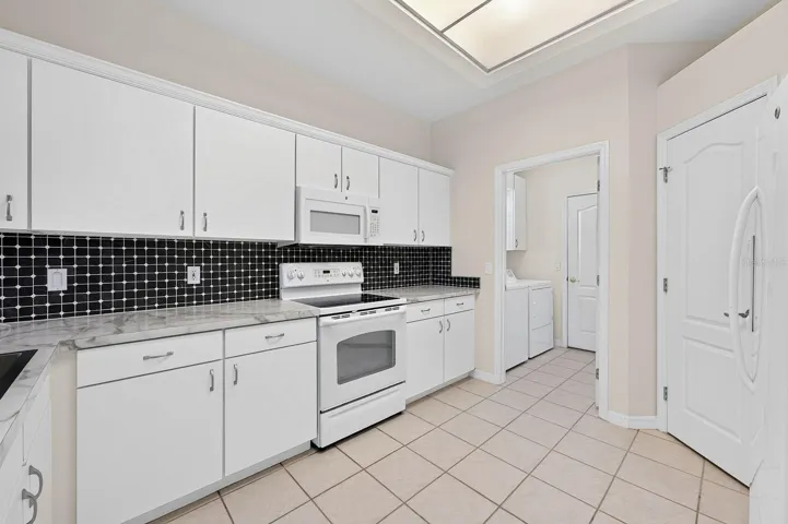 The spacious Kitchen, REFRESHED IN 2024, offers plenty to appreciate, including newer countertops, updated cabinet hardware and crown molding, a newer large sink and a tile backsplash.