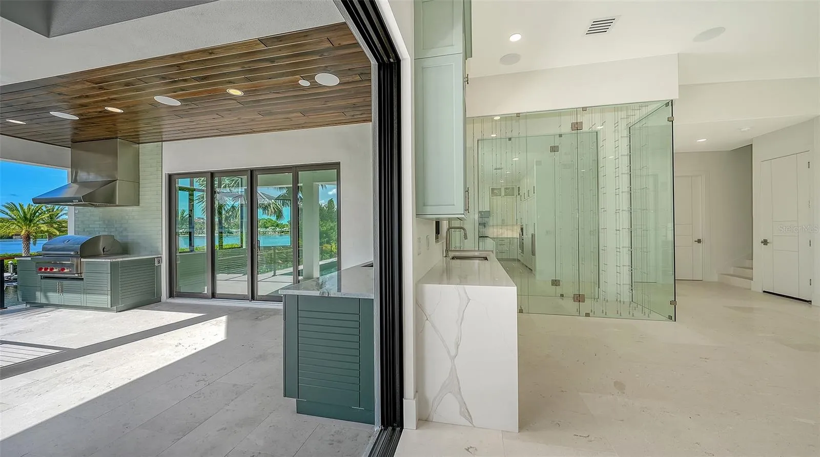 Disappearing pocketing glass doors create a seamless transition to the expansive outdoor living area, where a fully equipped summer kitchen, resort-style pool, and tranquil waterfront provide the ultimate setting for year-round entertaining.