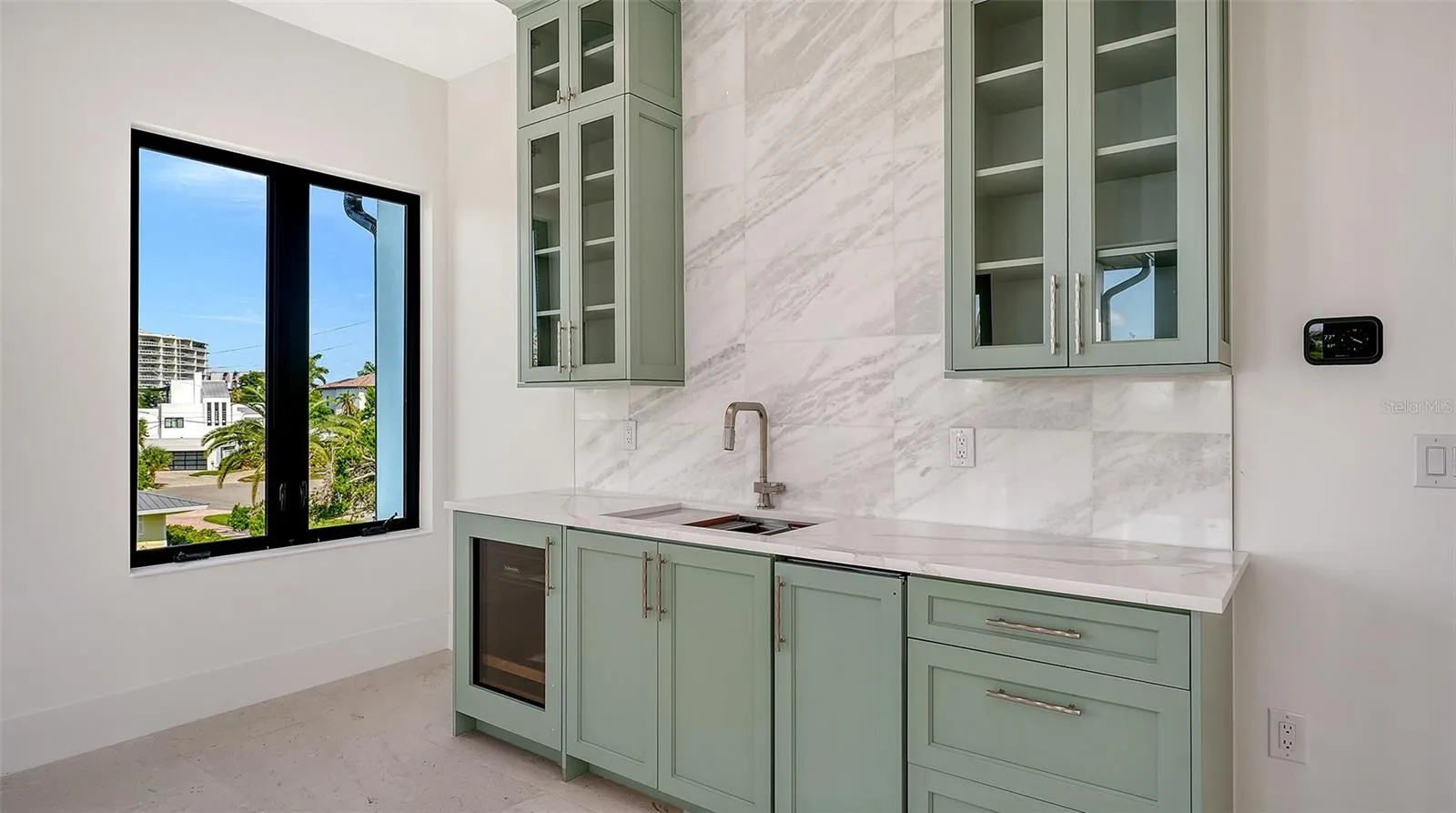 The thoughtfully designed beverage center features custom cabinetry, a full-height marble backsplash, a sink, and a built-in beverage refrigerator, making the top-floor bonus room ideal for effortless entertaining.
