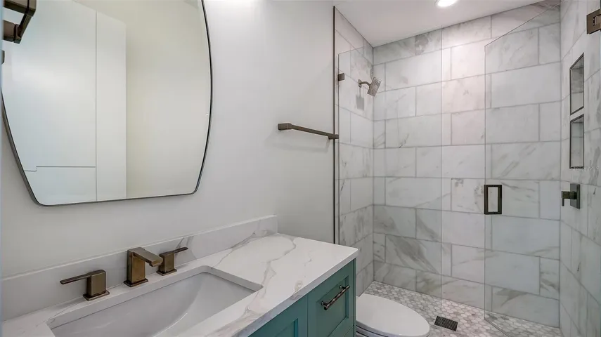 The top-level full bath is beautifully appointed with floor-to-ceiling marble, a frameless glass shower, designer fixtures, and custom cabinetry, offering a luxurious retreat for the adjacent bonus room and fourth room.