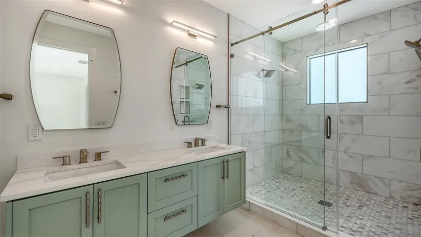 Designed with the same exceptional craftsmanship found throughout the home, the second primary bath offers dual vanities, floor-to-ceiling marble, and an expansive walk-in shower featuring four independently controlled shower fixtures.