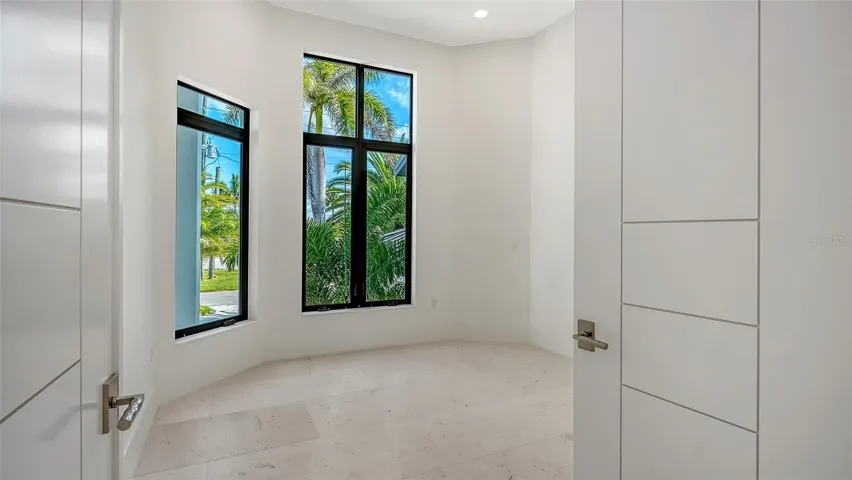 With the abundance of natural light, the private office combines floor-to-ceiling PGT impact windows with solid TruStile French doors, creating a serene, exceptionally quiet workspace with lush tropical views.