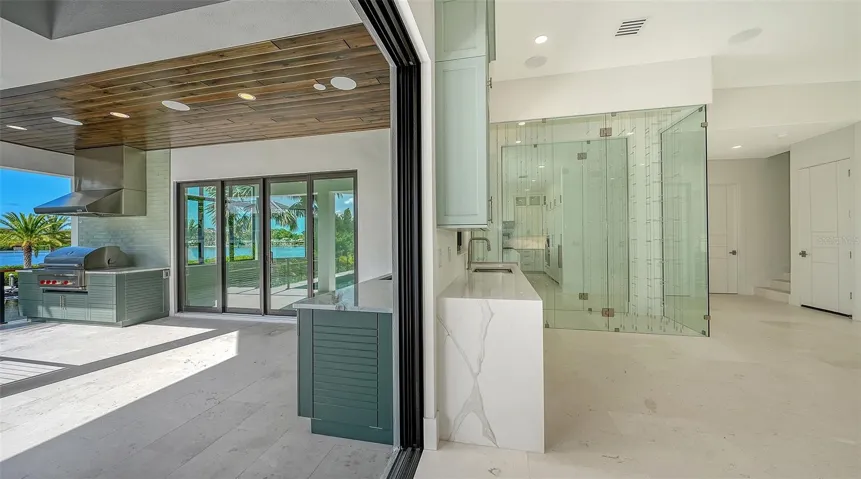 Disappearing pocketing glass doors create a seamless transition to the expansive outdoor living area, where a fully equipped summer kitchen, resort-style pool, and tranquil waterfront provide the ultimate setting for year-round entertaining.