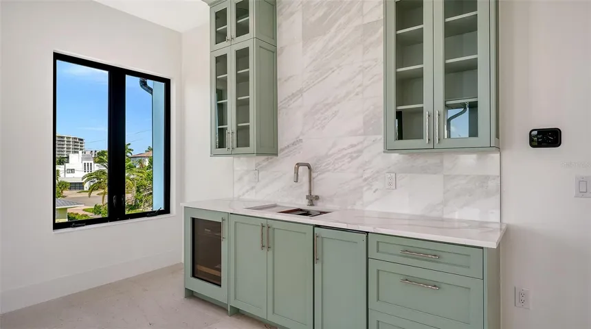 The thoughtfully designed beverage center features custom cabinetry, a full-height marble backsplash, a sink, and a built-in beverage refrigerator, making the top-floor bonus room ideal for effortless entertaining.