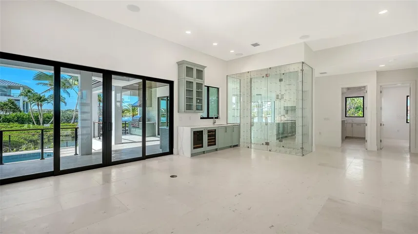 Grand great room featuring soaring ceilings, walls of pocketing glass, a custom beverage bar, and effortless indoor-outdoor living overlooking the pool and waterfront.