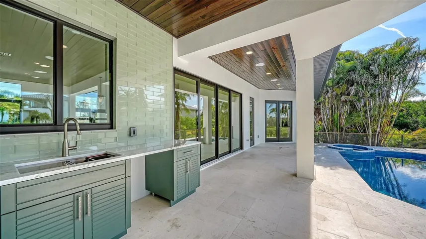 The covered lanai showcases a custom outdoor prep kitchen with generous counter space, built-in cabinetry, and a sink, thoughtfully designed to complement the adjacent summer kitchen and create the ultimate outdoor entertaining experience.