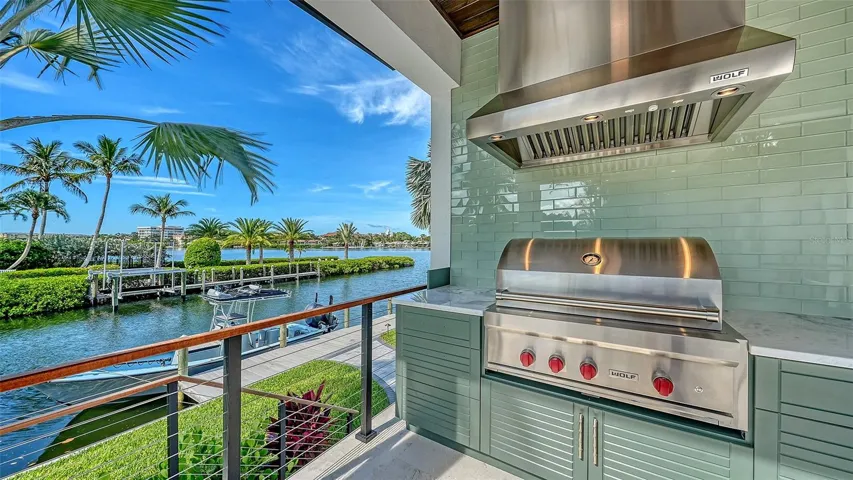 The covered summer kitchen features a premium Wolf grill, professional-grade vent hood, custom cabinetry, and expansive prep space, all perfectly positioned to capture breathtaking waterfront views while creating an exceptional outdoor entertaining experience.