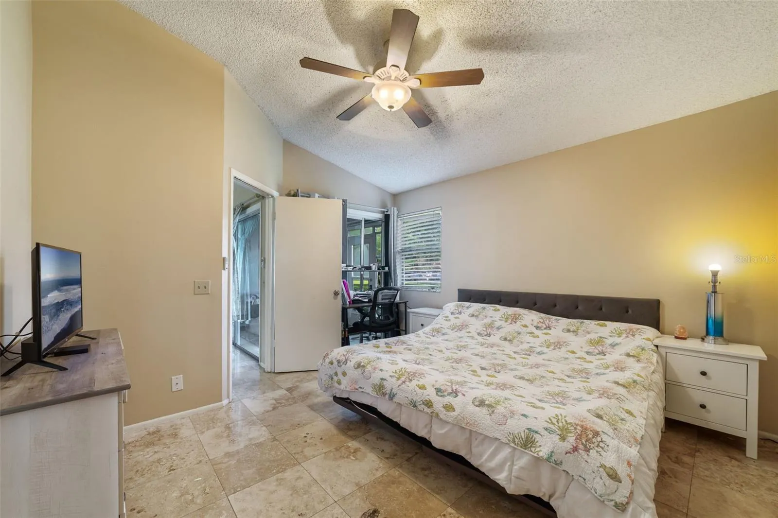Spacious primary bedroom with sliding door access to the screened in patio, a ceiling fan, and vaulted ceilings