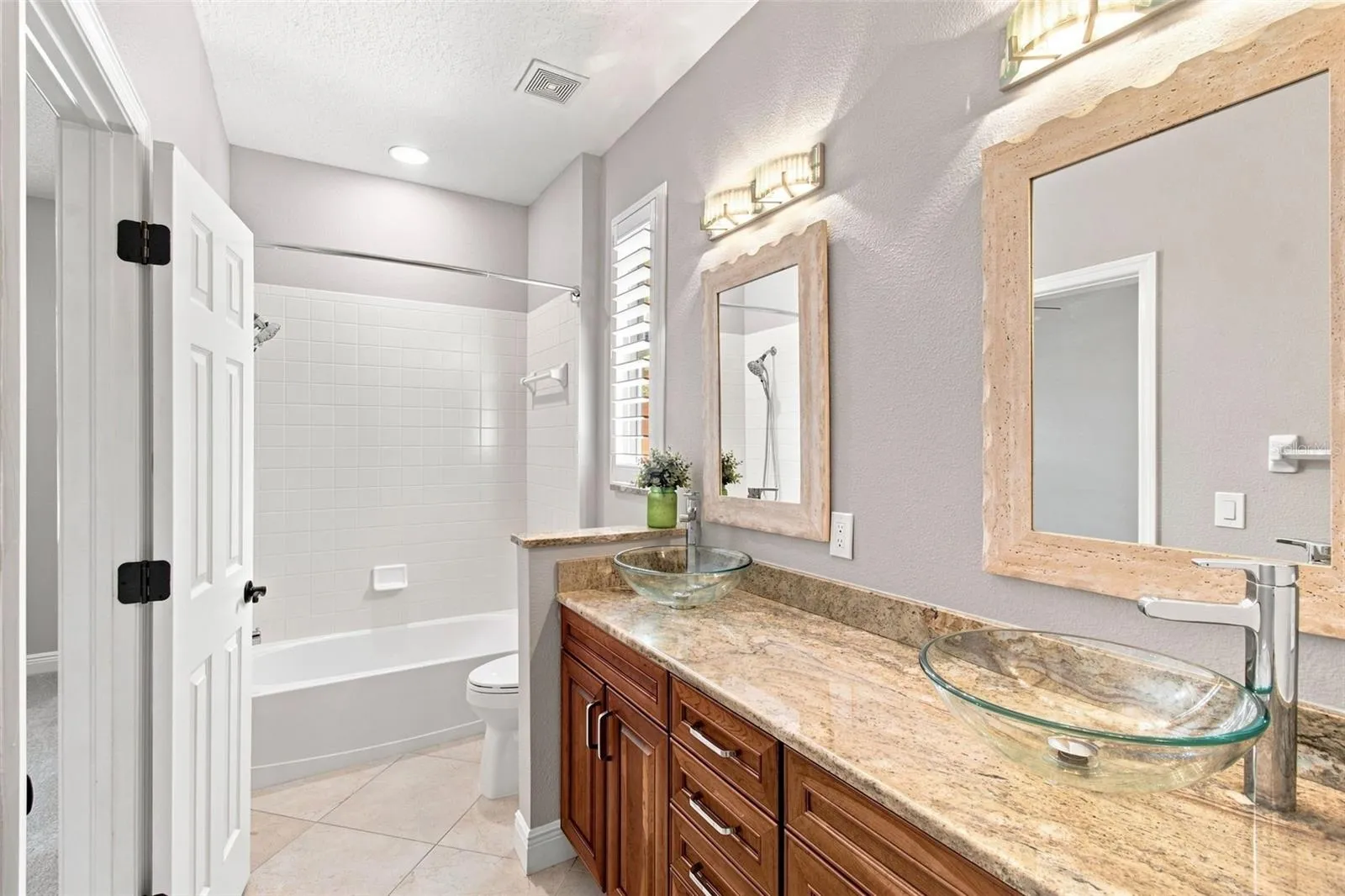 Jack &amp; Jill bathroom with upgraded granite, dual glass sinks, soft-close cabinet doors and drawers, plantation shutters and a linen closet.