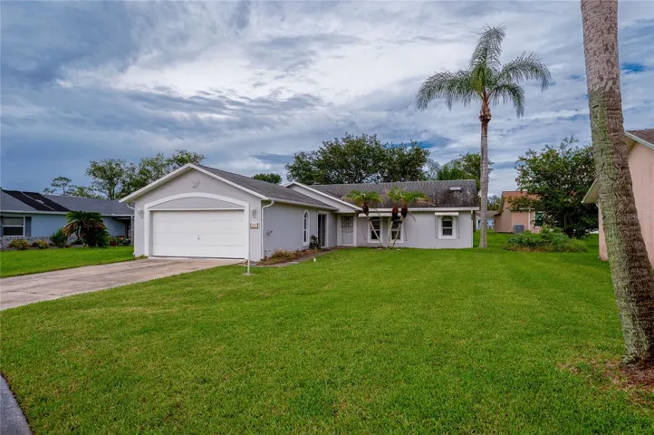 Front perspective of the home displaying a spacious front yard, two-car garage, concrete driveway, and palm trees.