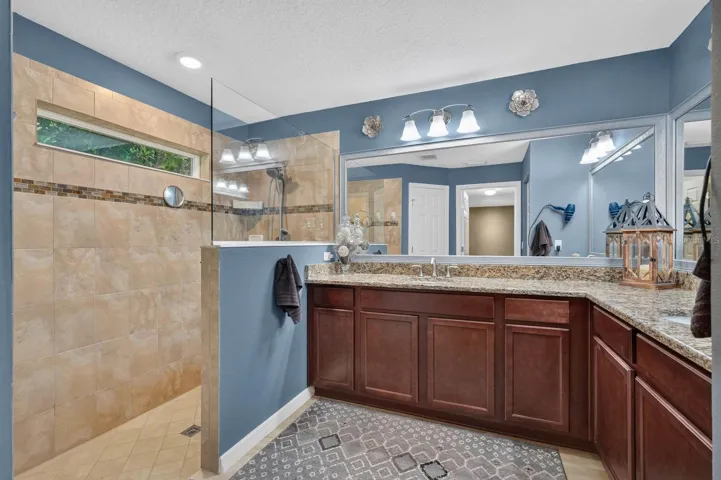 Primary bathroom features tiled showers, granite countertops, wood cabinetry