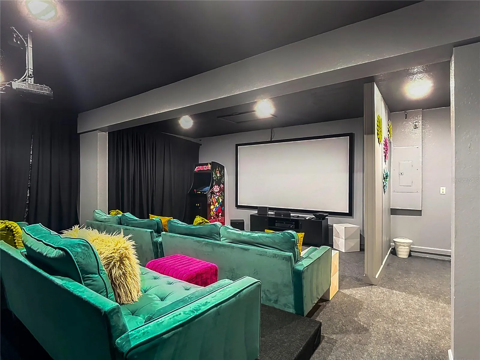 Dedicated theater room with oversized seating, projector, aracde machine and cinema screen.
