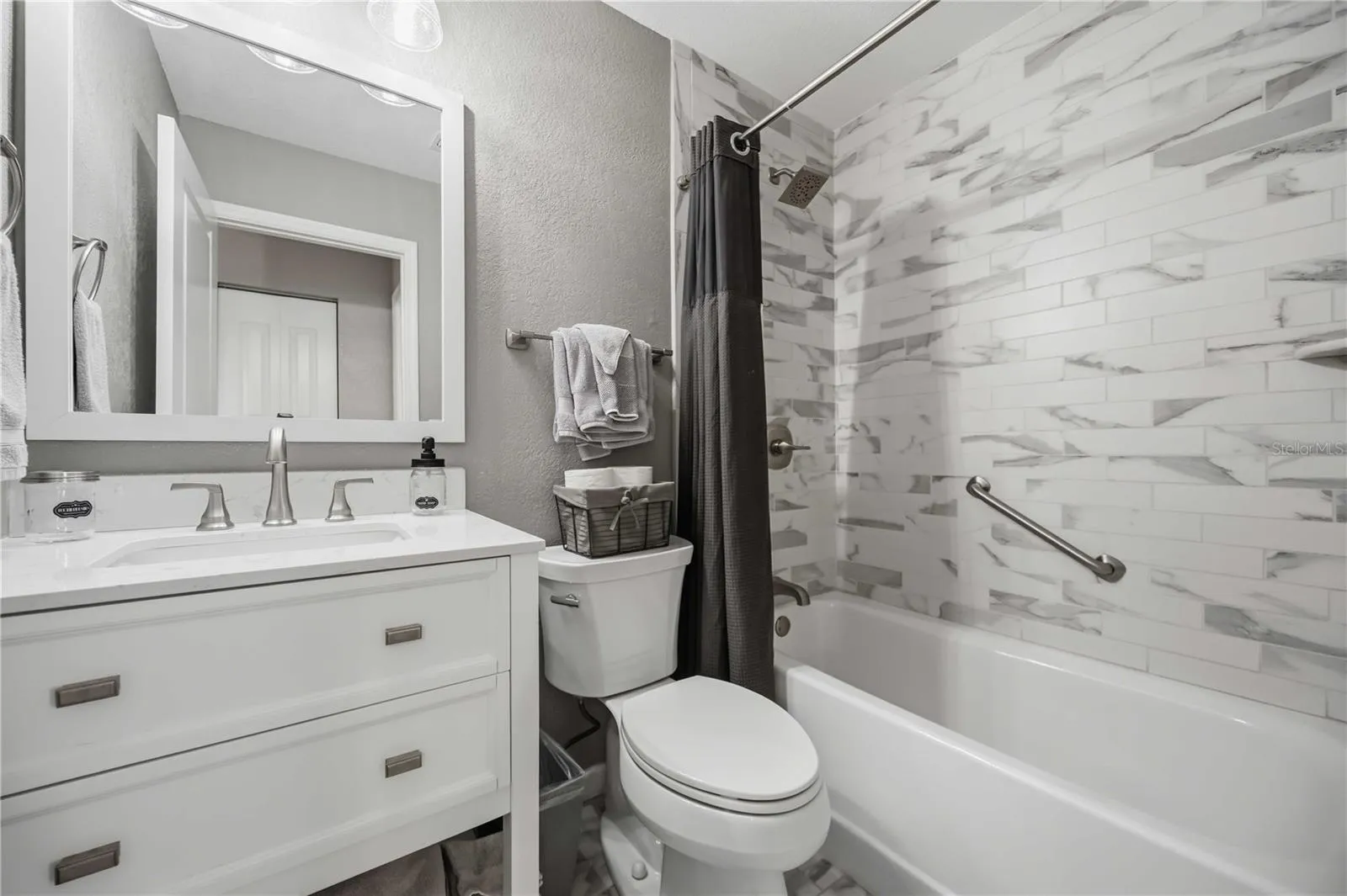 Updated guest bath features a clean white vanity and a beautifully tiled tub-and-shower surround.