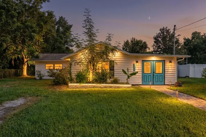Front Elevation Charming single-story facade featuring distinct turquoise double entry doors, a raised stone planter box, and a spacious green lawn.