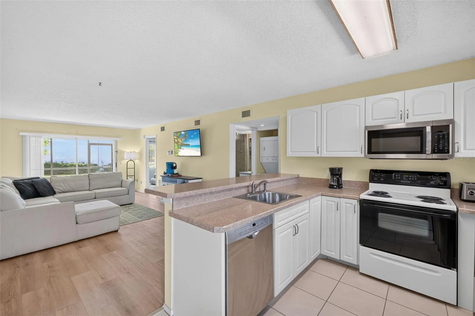 Kitchen featuring a Tile Floor, Dishwasher, Stove, Microwave overlooking the Living/Dining Area and Sliding Glass Doors to the Screened Lanai